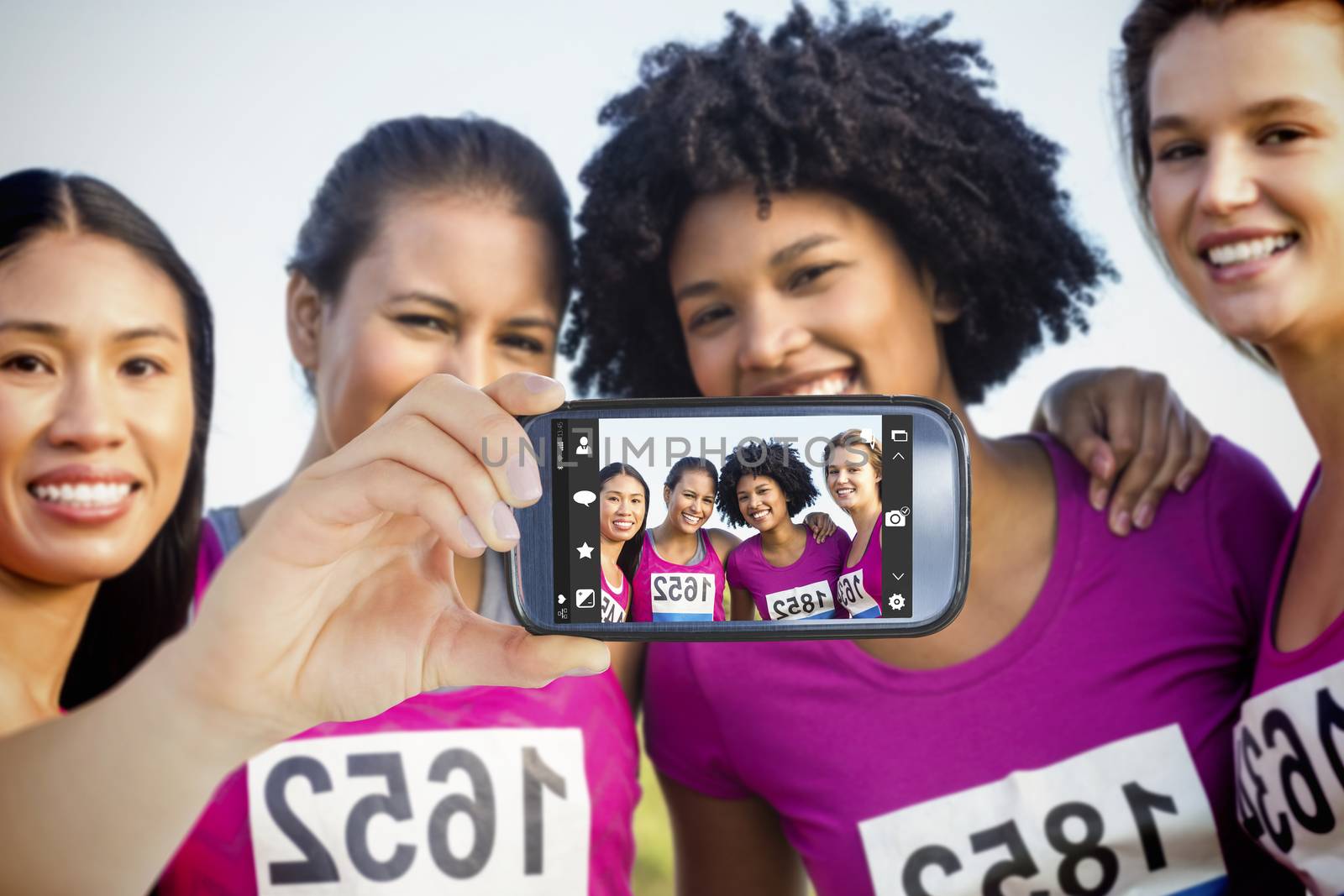 Hand holding smartphone showing against four smiling runners supporting breast cancer marathon