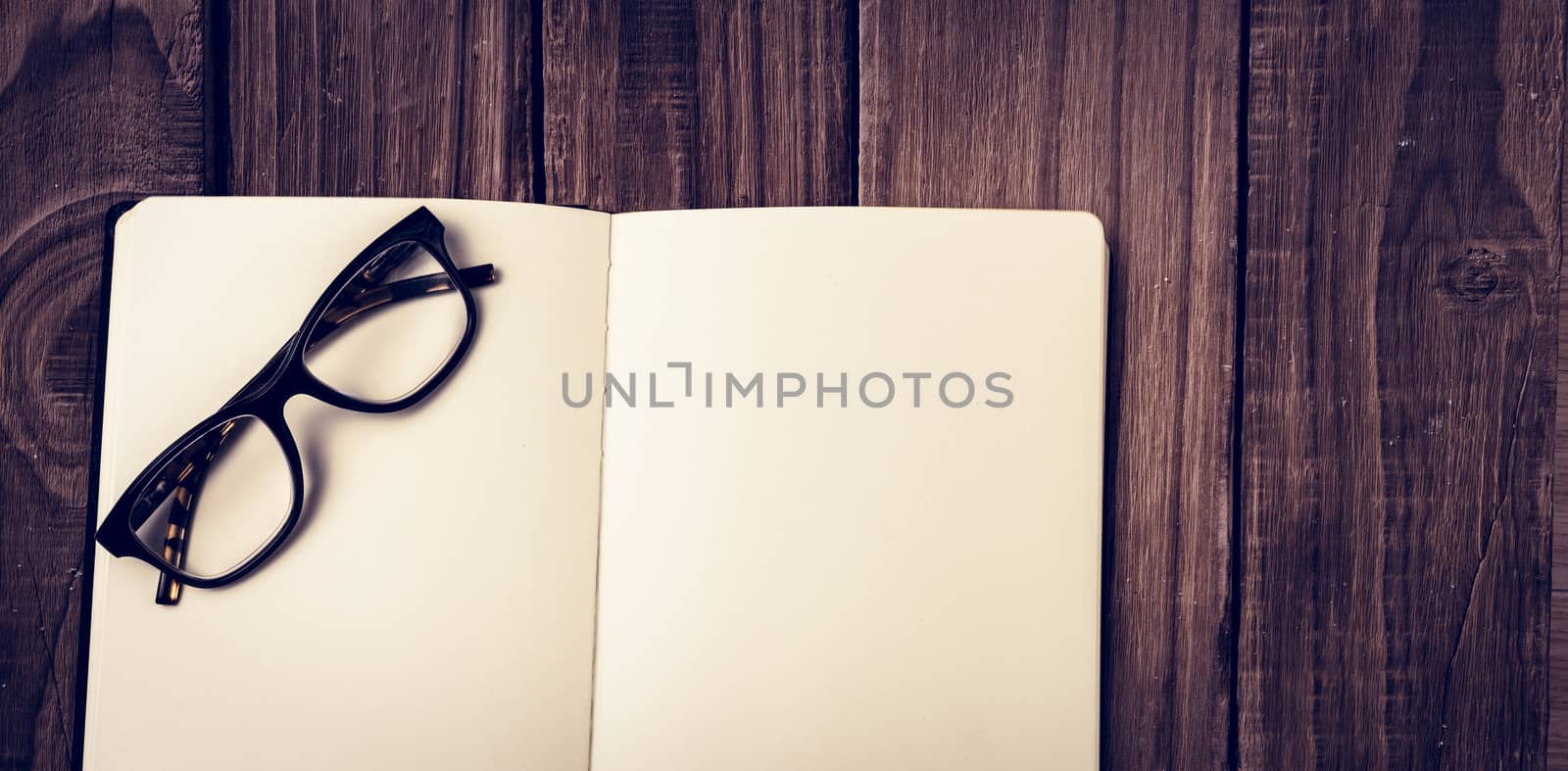 Overhead view of reading glasses on blank book against wooden table