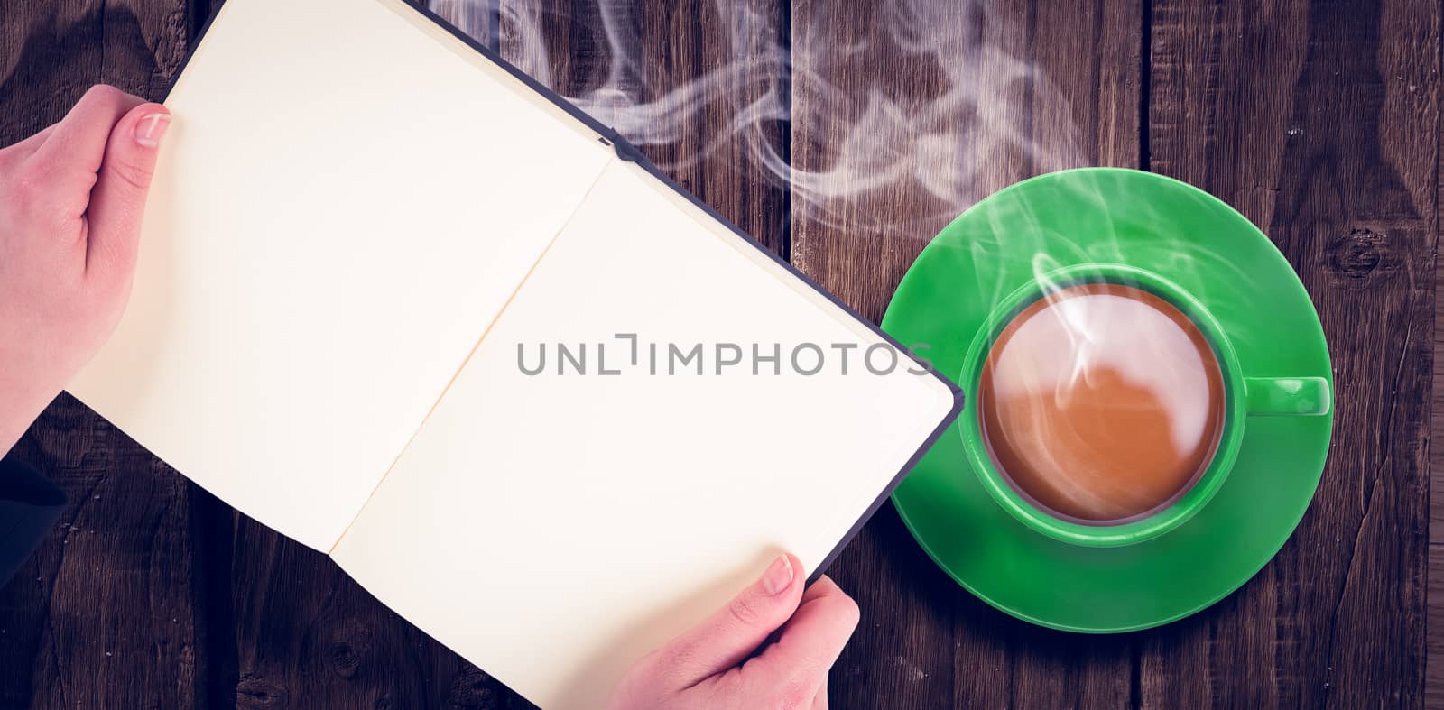 Overhead view of hot tea by hand holding book over wooden table