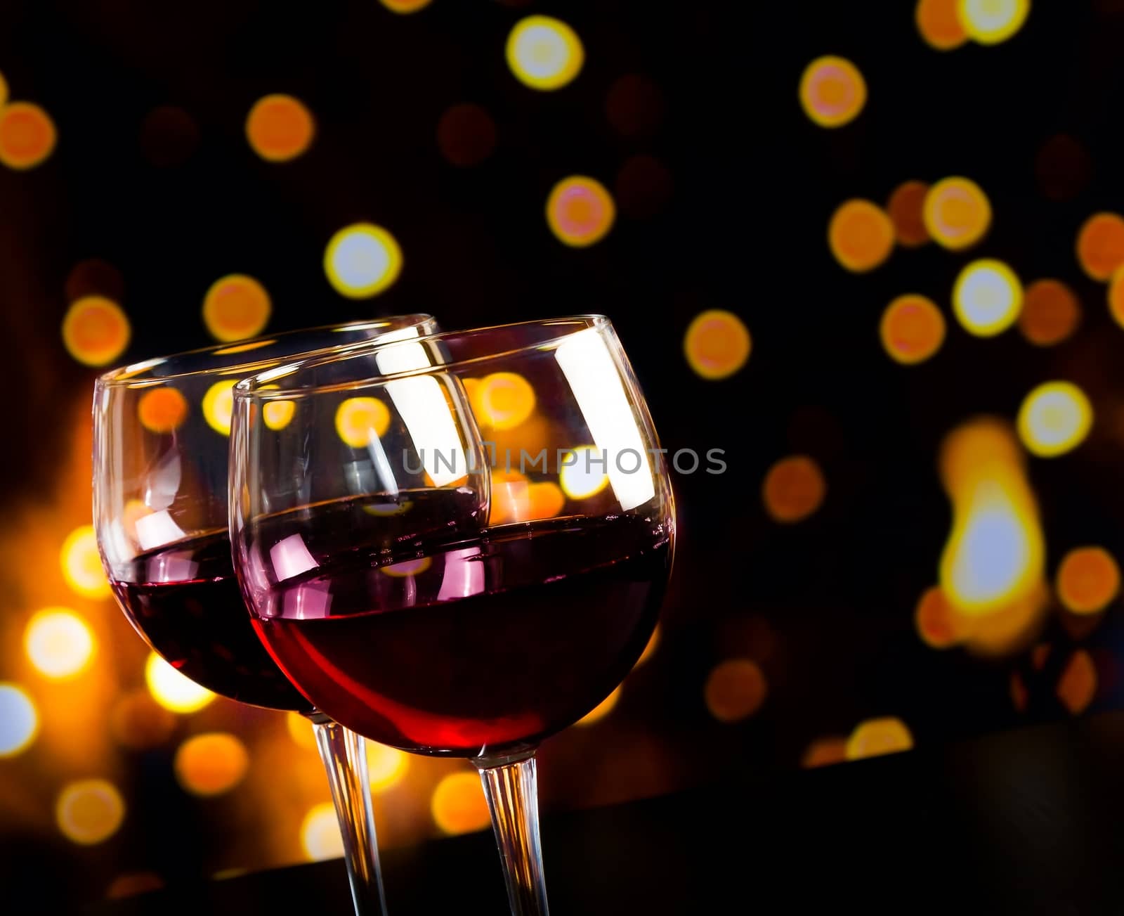 two red wine glasses on wood table against bokeh lights background by donfiore