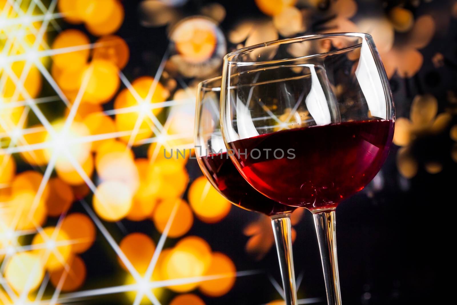 two red wine glasses against golden bokeh lights background, festive and fun concept