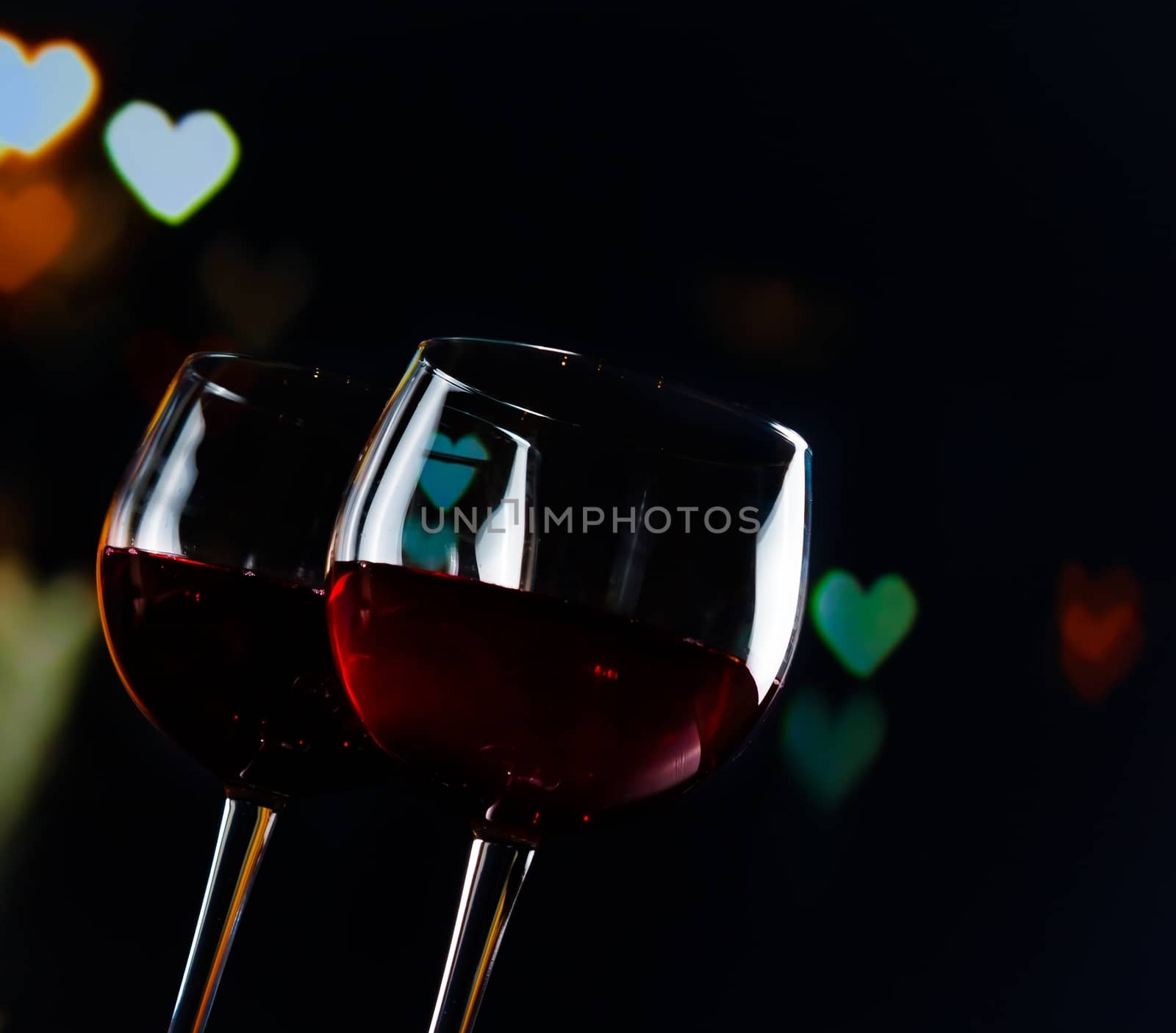 two red wine glasses on hearts decoration bokeh lights background by donfiore