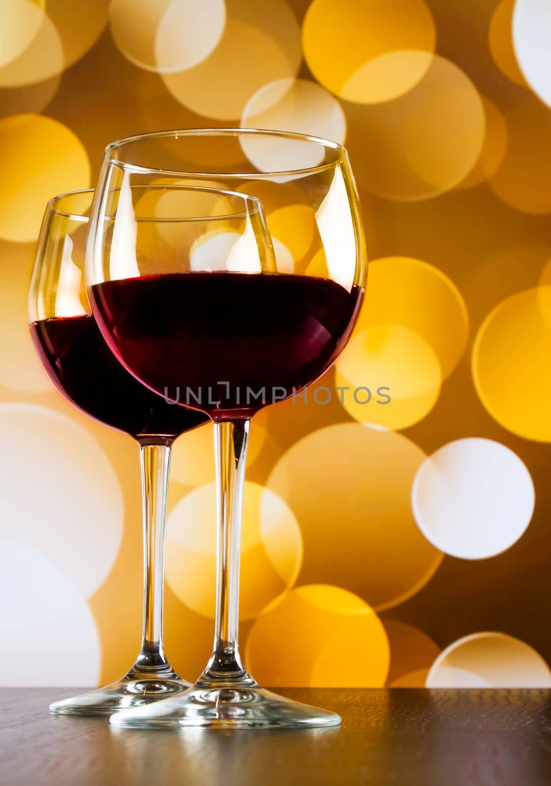 red wine glasses on wood table against golden bokeh lights background by donfiore