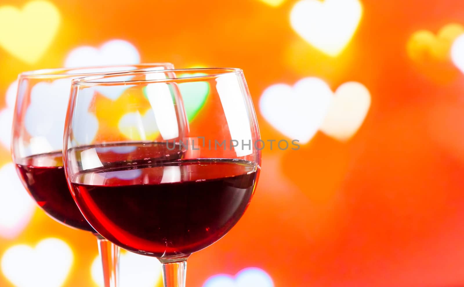 two red wine glasses on hearts decoration bokeh lights background, festive and love concept