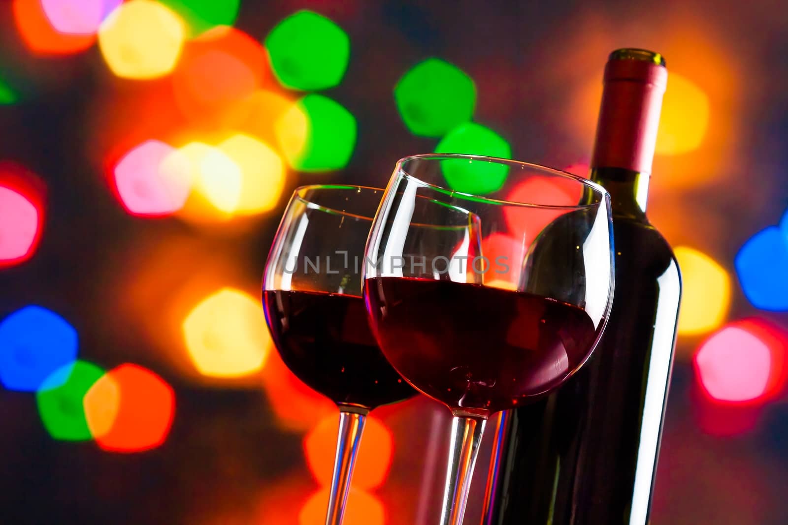 two red wine glasses near bottle against colorful bokeh lights background, festive and fun concept