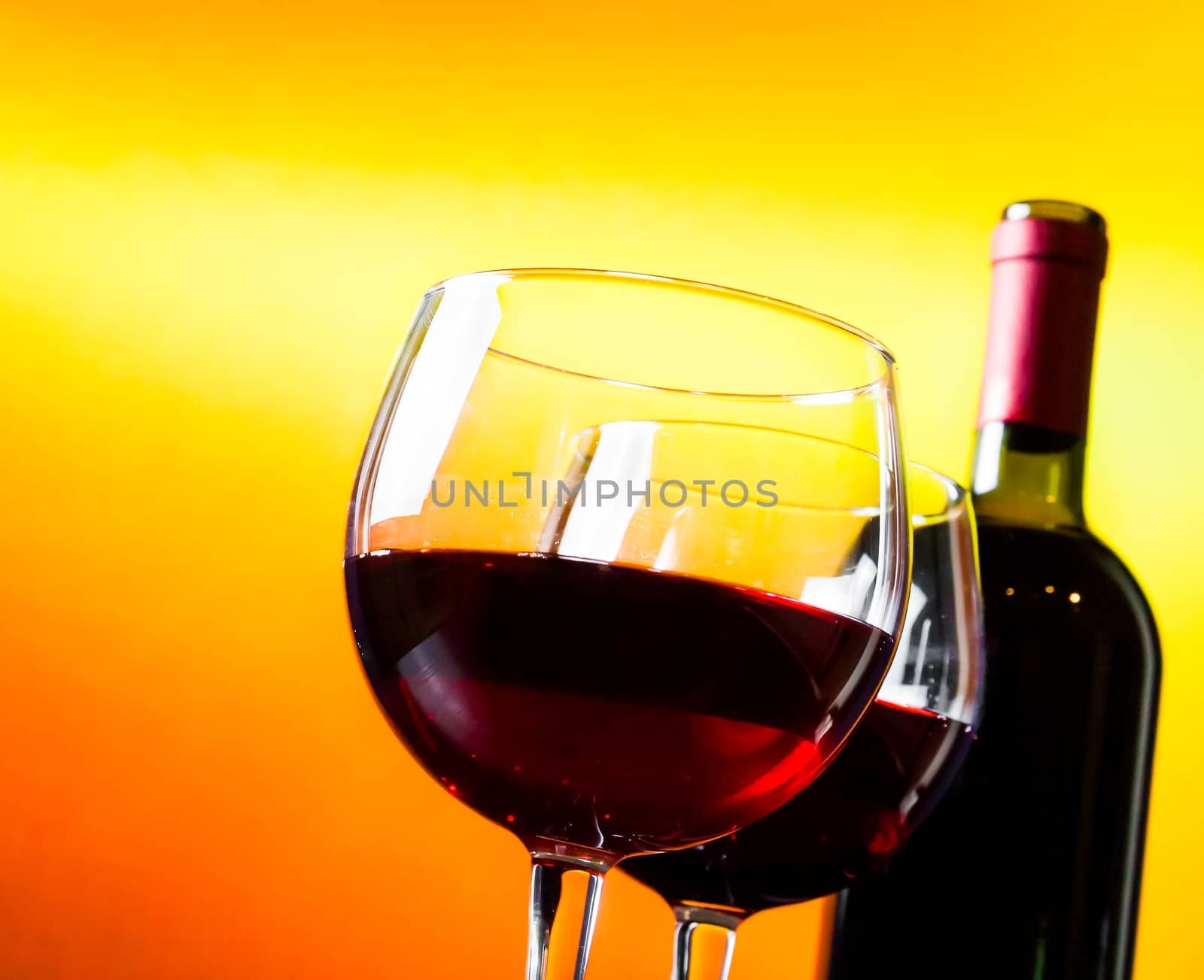 two red wine glasses near the bottle against golden lights background, festive and fun concept