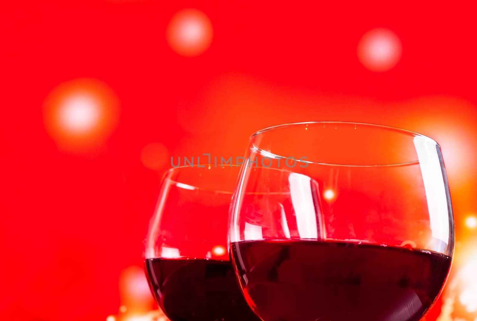 two red wine glasses near the bottle against red lights background, festive and fun concept