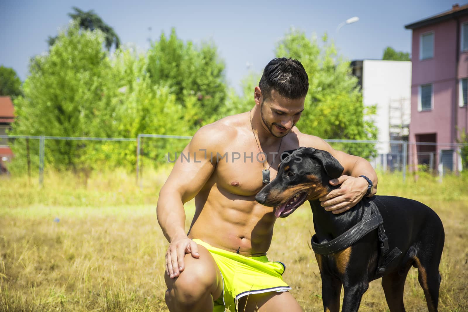 Half Body Shot of a Shirtless Athletic Young Man with his Dog and Looking at It