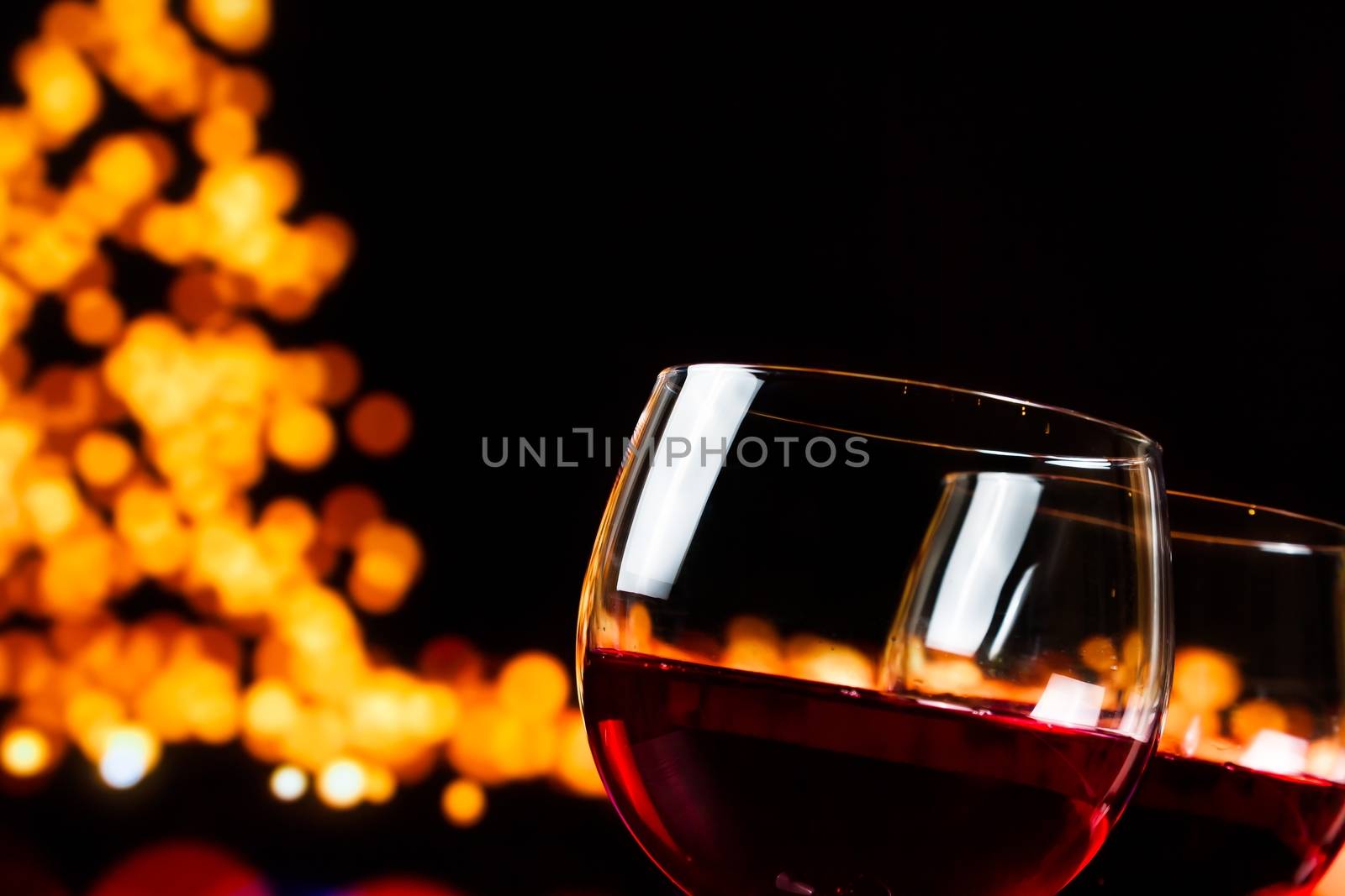 two red wine glasses against tree of bokeh lights background, christmas atmosphere