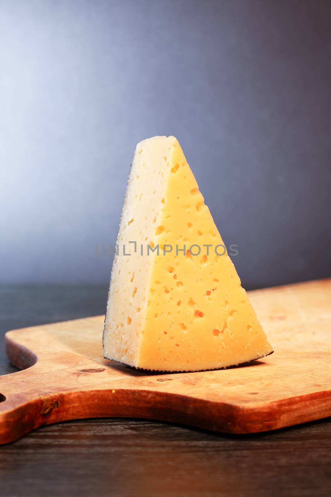 Piece of  hard cheese on wooden cutting board