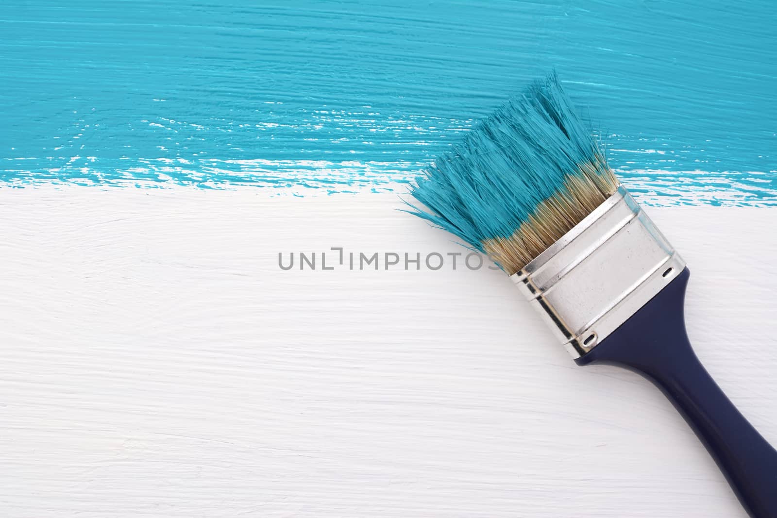 Horizontal stripe of turquoise paint with a dirty paintbrush on a white wooden board