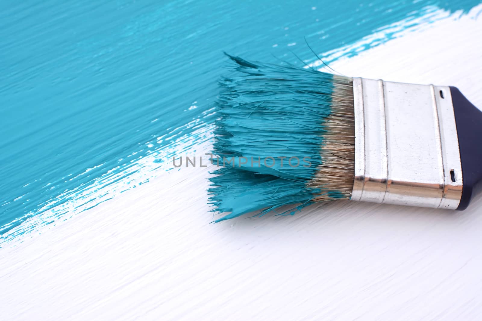 Close-up of paintbrush with paint-covered bristles painting a white board blue