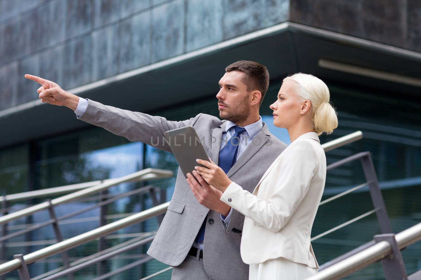 business, partnership, technology and people concept - serious businessman and businesswoman with tablet pc computer over office building