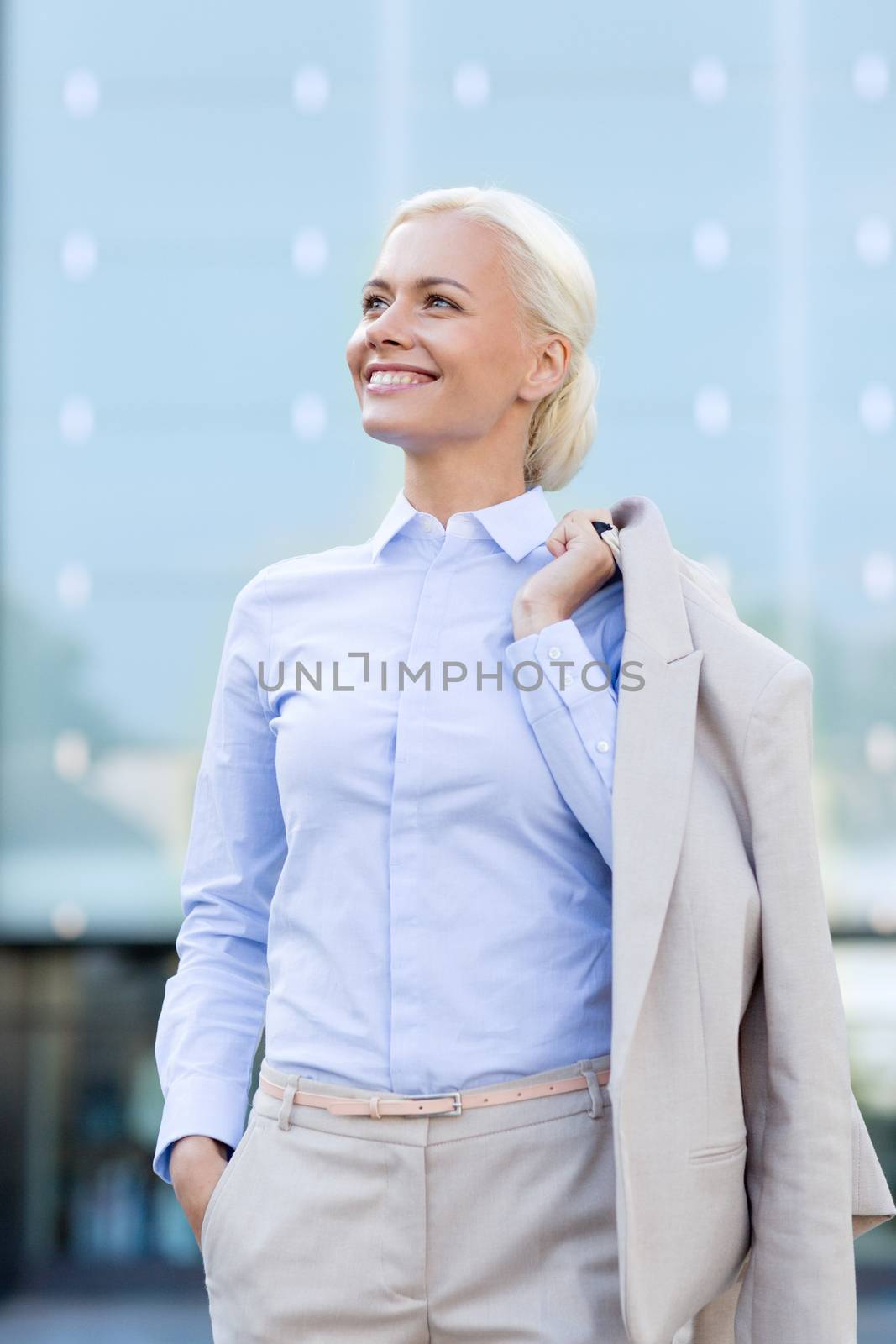 business, people and education concept - young smiling businesswoman over office building