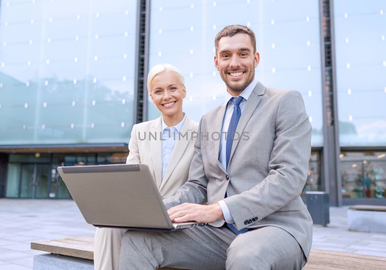 business, education, technology and people concept - smiling businesspeople working with laptop computer on city street