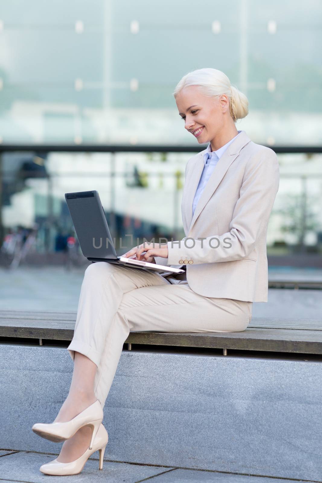 business, education, technology and people concept - smiling businesswoman working with laptop computer on city street