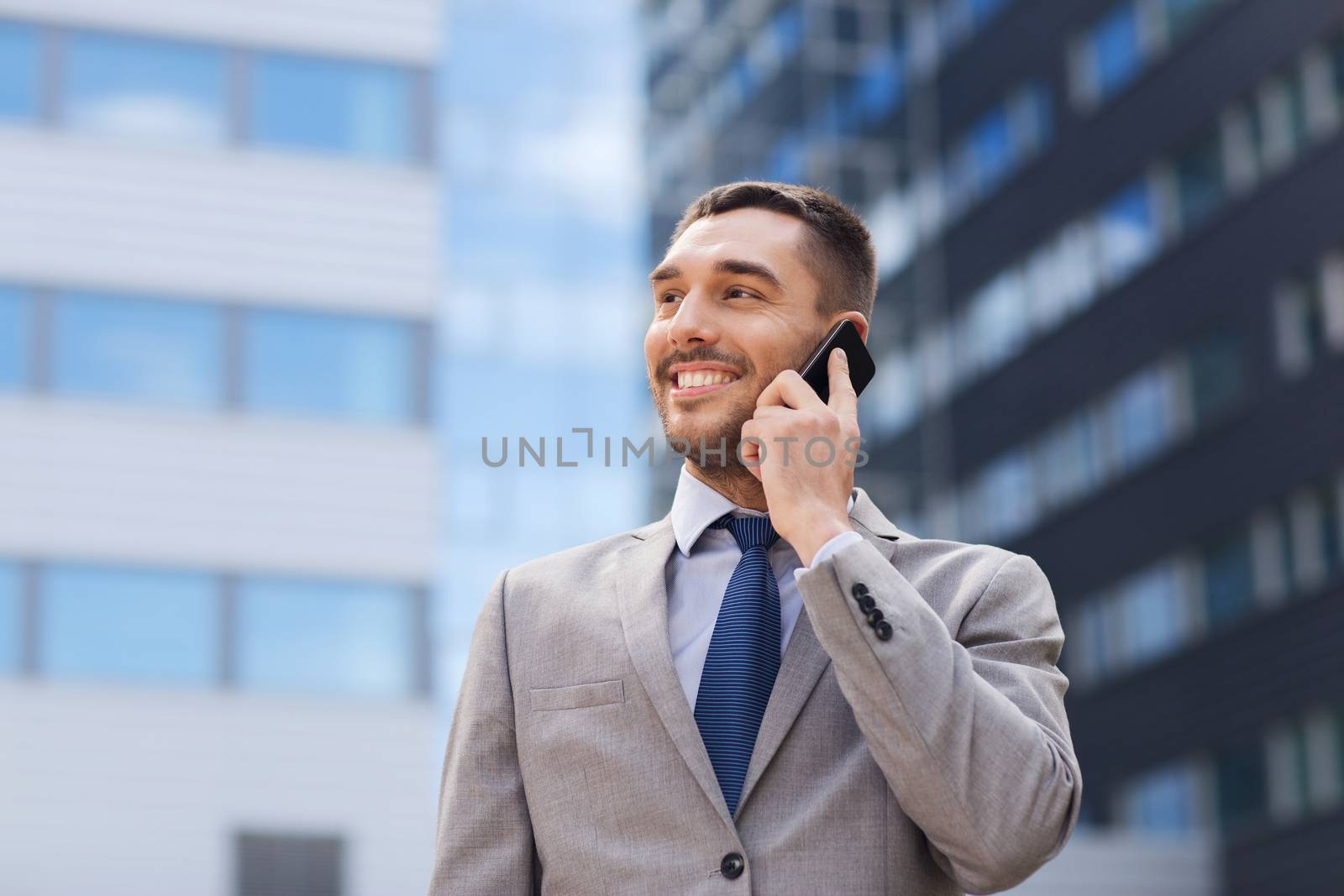 business, technology and people concept - smiling businessman with smartphone talking over office building