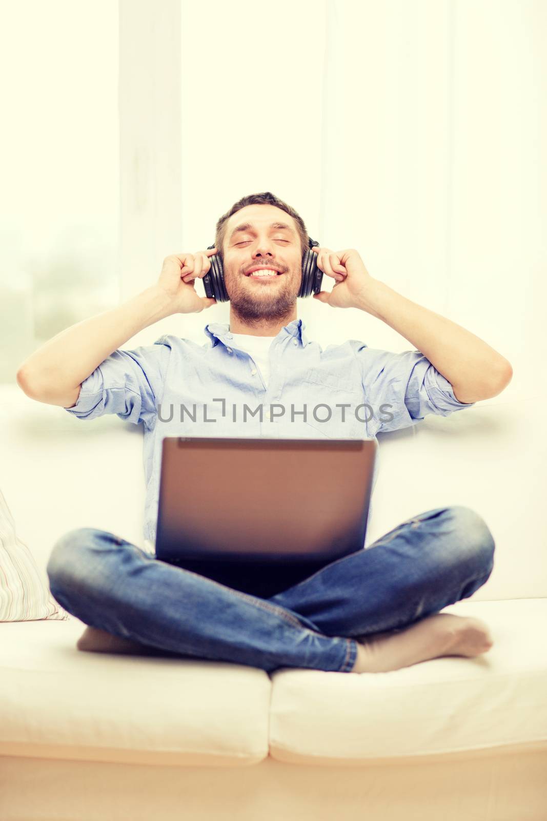 smiling man with laptop and headphones at home by dolgachov