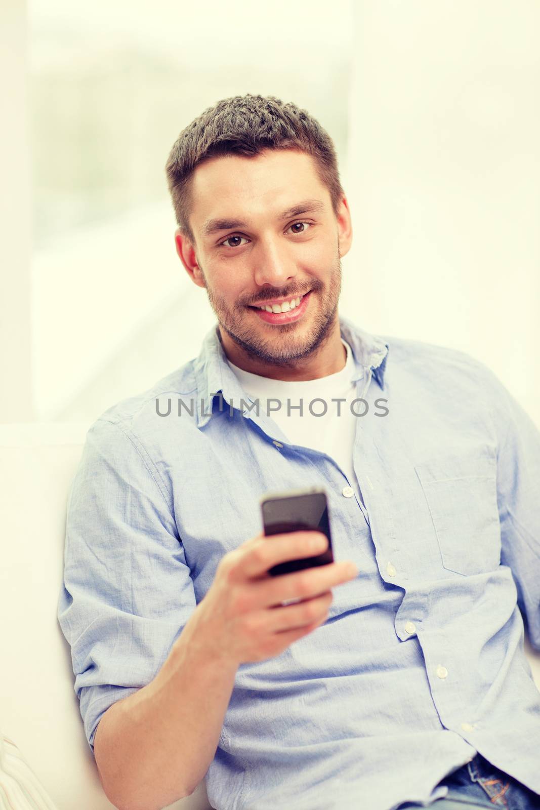 smiling man with smartphone at home by dolgachov