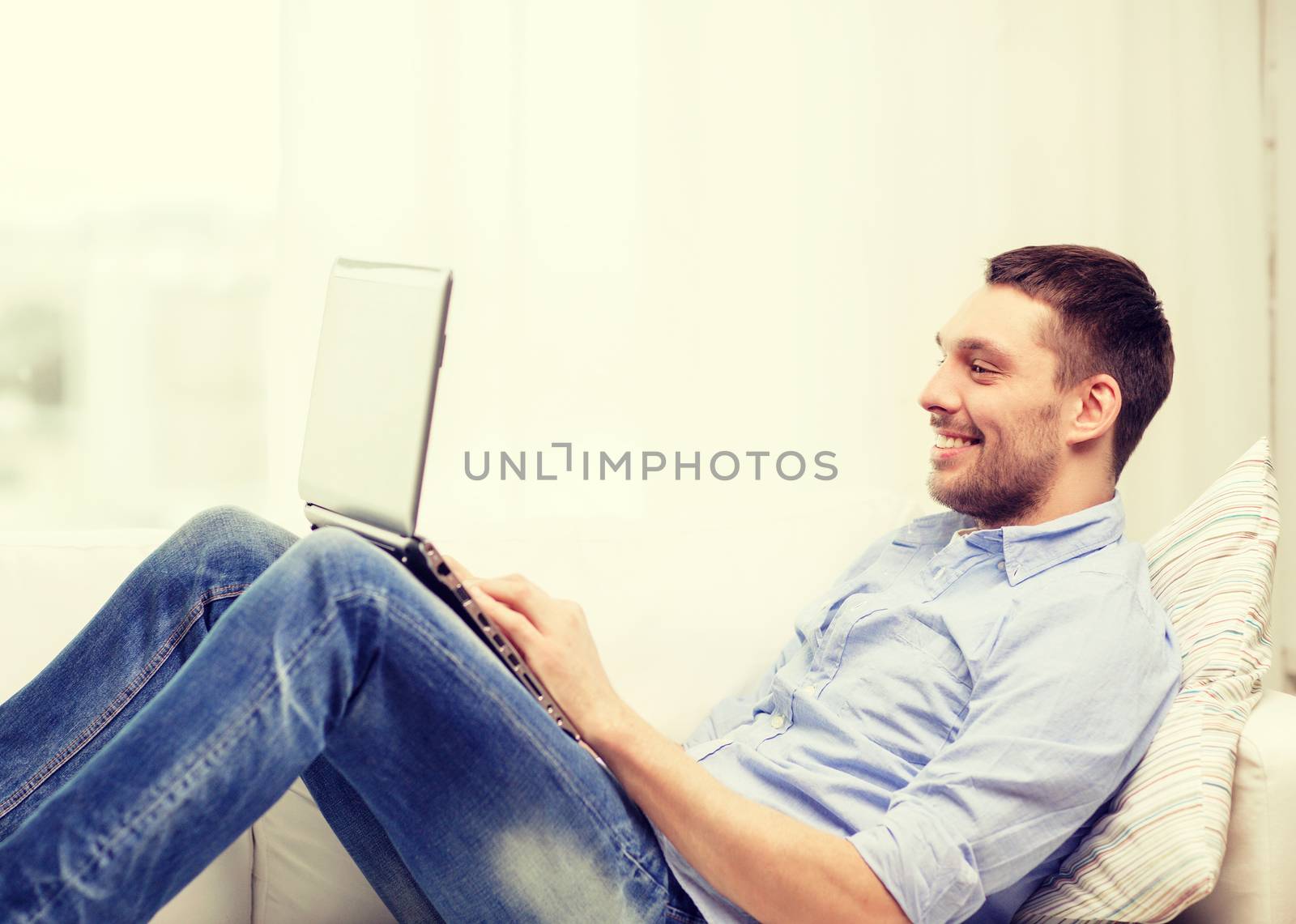 smiling man working with laptop at home by dolgachov