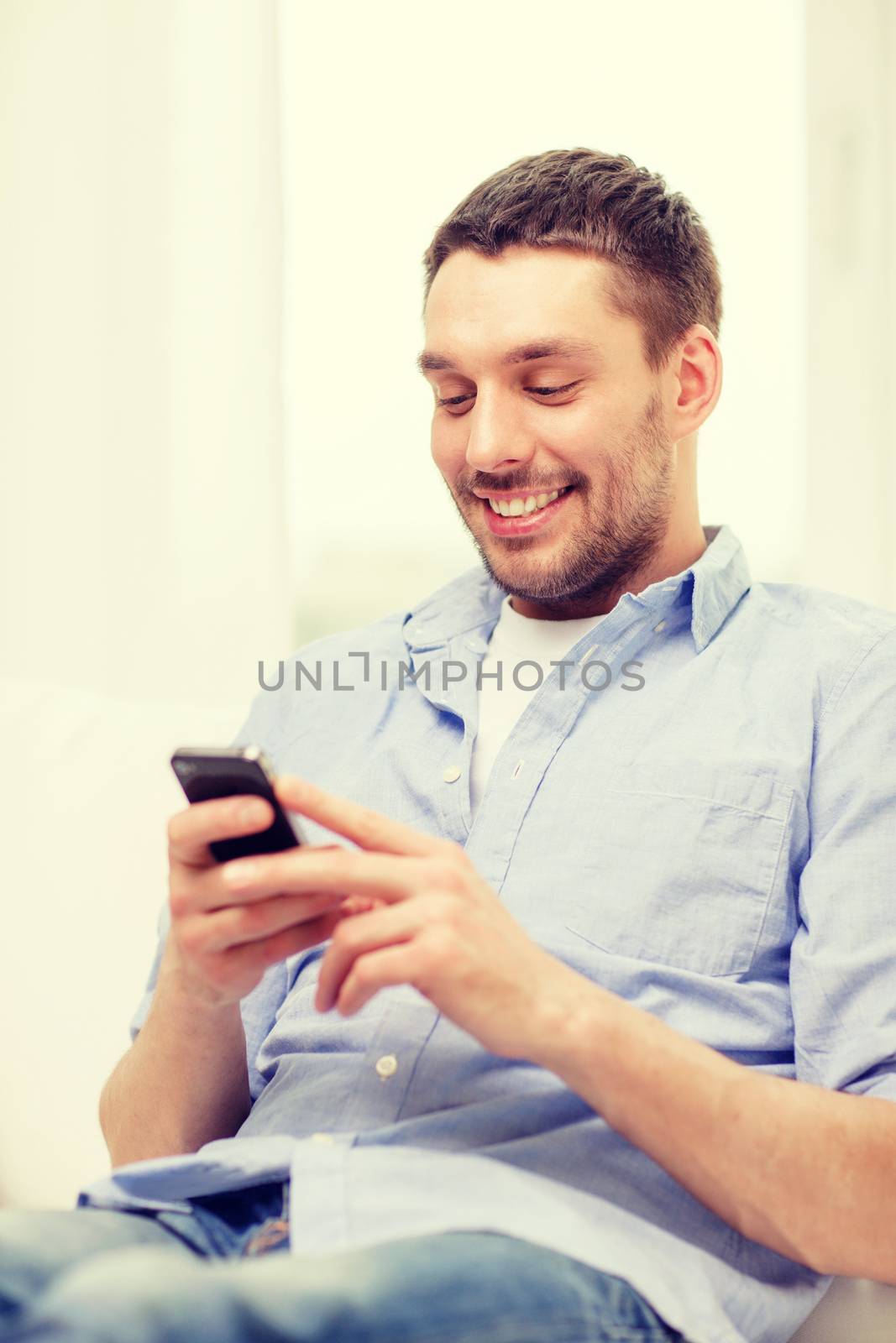 home, technology and internet concept - smiling man with smartphone sitting on couch at home