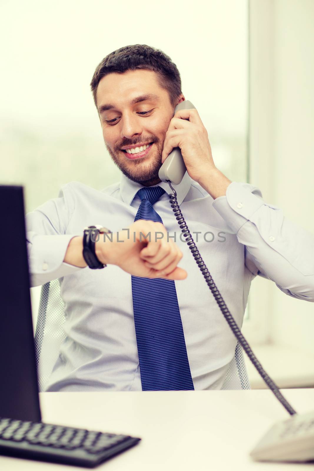business, office and technology concept - smiling businessman making call and looking at wristwatch at office