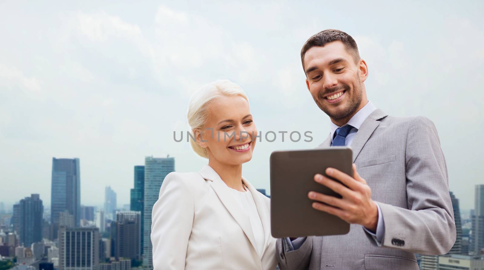 business, partnership, technology and people concept - smiling businessman and businesswoman with tablet pc computer over city background