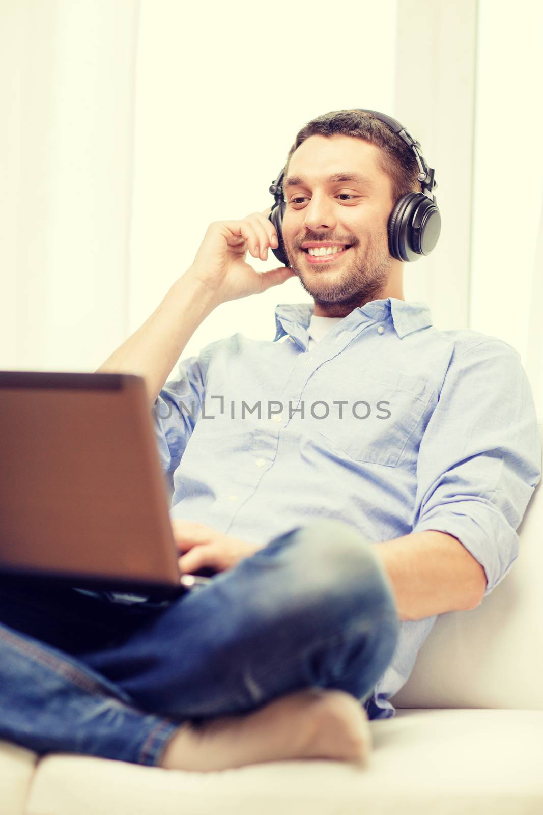 smiling man with laptop and headphones at home by dolgachov