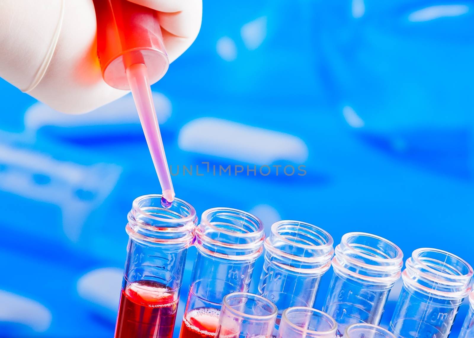 hand with pipette on test tubes with red liquid in laboratory on blue light tint background