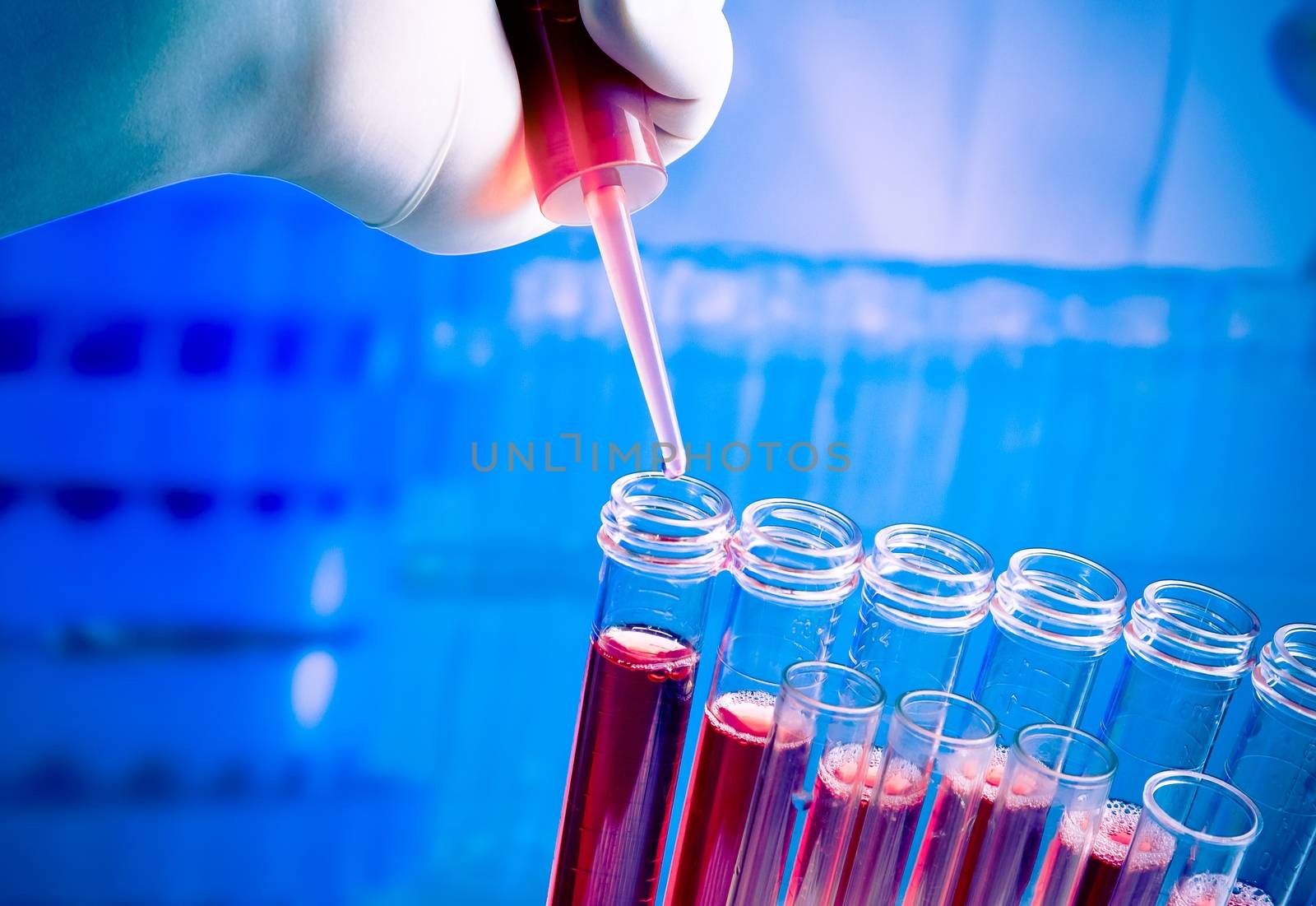 hand with pipette on test tubes with red liquid in laboratory on blue light tint background