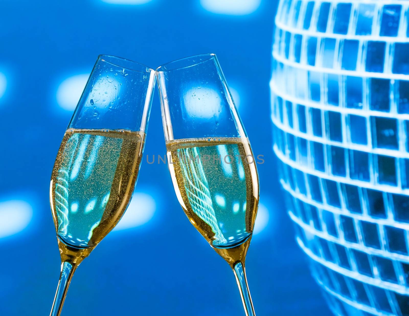 a pair of champagne flutes with golden bubbles make cheers on sparkling blue disco ball background by donfiore