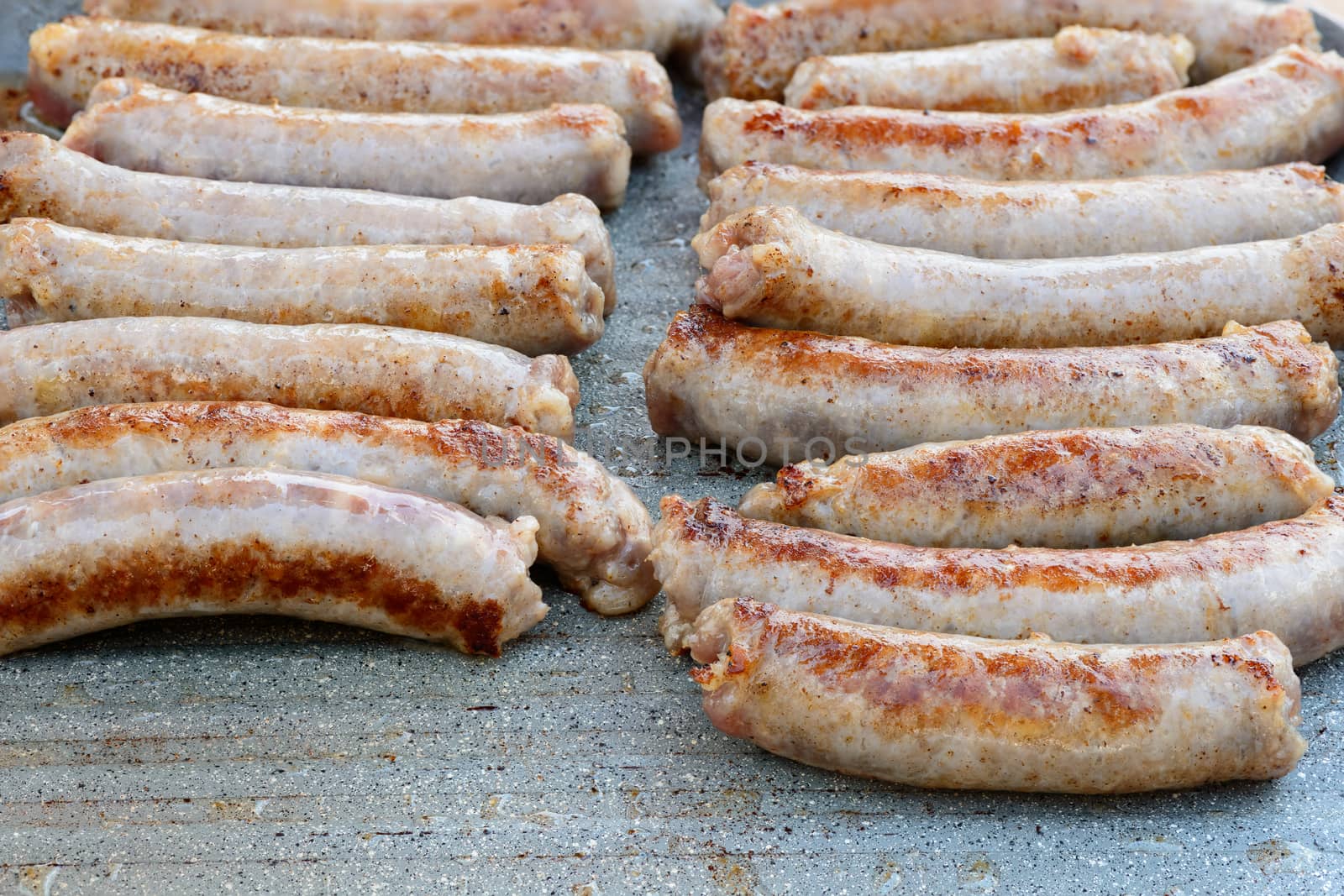 Pictured pork sausages placed in two vertical rows are cooked on the grill.