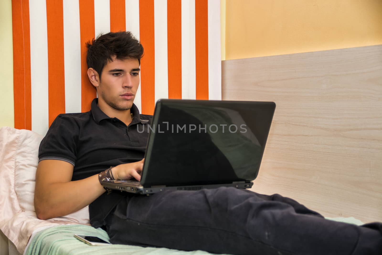 Young Man Doing Homework on Laptop in Bedroom by artofphoto