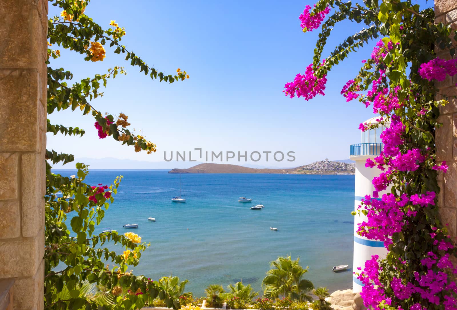 Beautiful flowers can be seen past the Lighthouse at Ortakent in Turkey with blue/green seas stretching to the horizon.