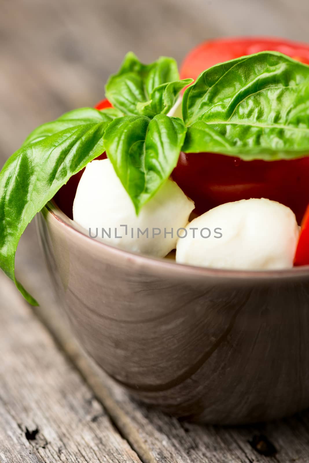 Tomato and mozzarella with basil leaves in bowl on wooden table