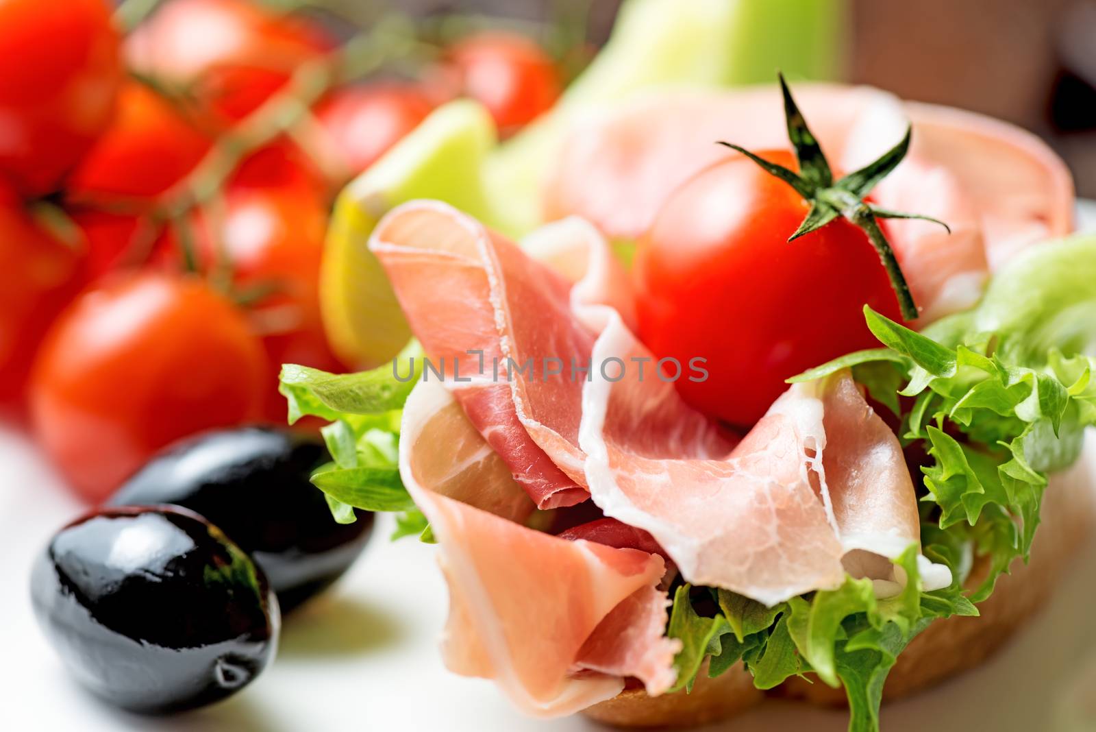 thin slices of prosciutto with olives and tomato on plate close  by Nanisimova