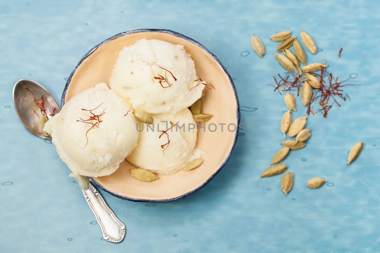 Saffron and Cardamom Ice Cream in small bowl over blue table. Macro photograph with shallow depth of field. Top view