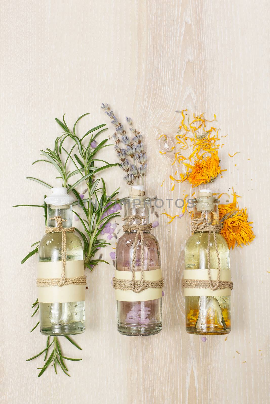 Row of essential oils in glass bottles, rosemary, lavender and calendula, on the wooden board.