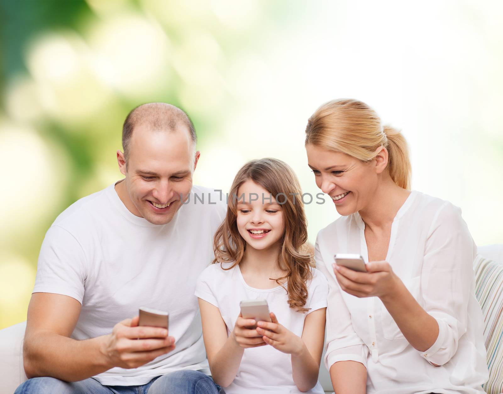 family, summer, technology and people - smiling mother, father and little girl with smartphones over green background