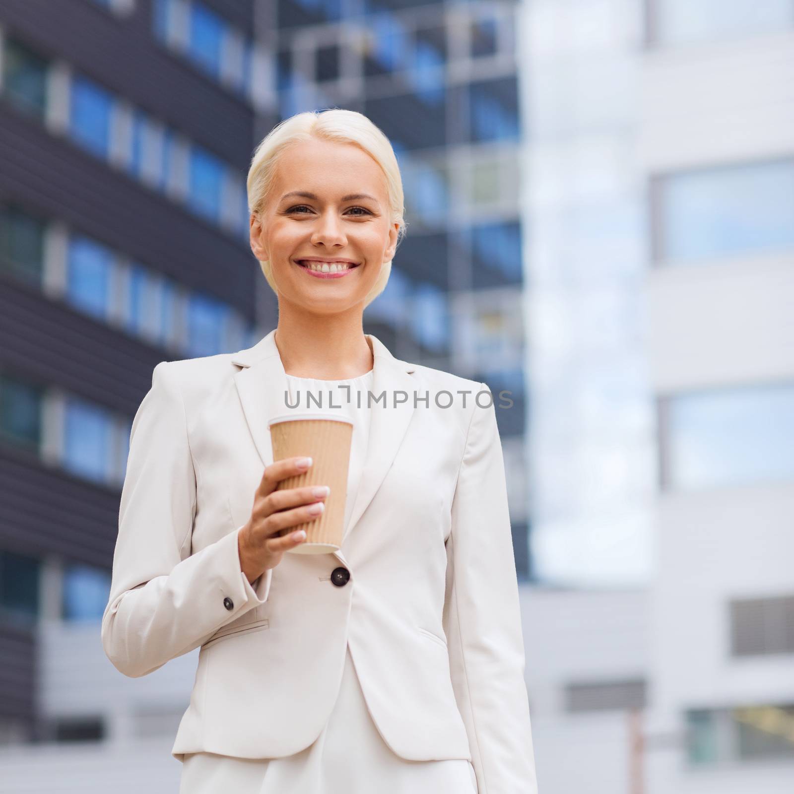 business, hot drinks and people and concept - young smiling businesswoman with paper coffee cup over office building
