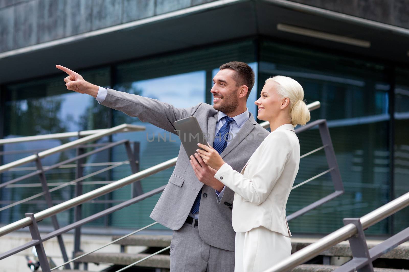 business, partnership, technology and people concept - smiling businessman and businesswoman with tablet pc computer over office building