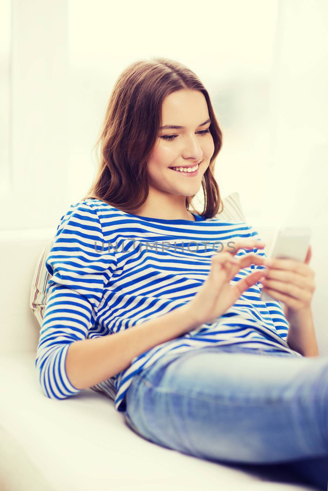 home, technology and internet concept - smiling teenage girl with smartphone lying on couch at home