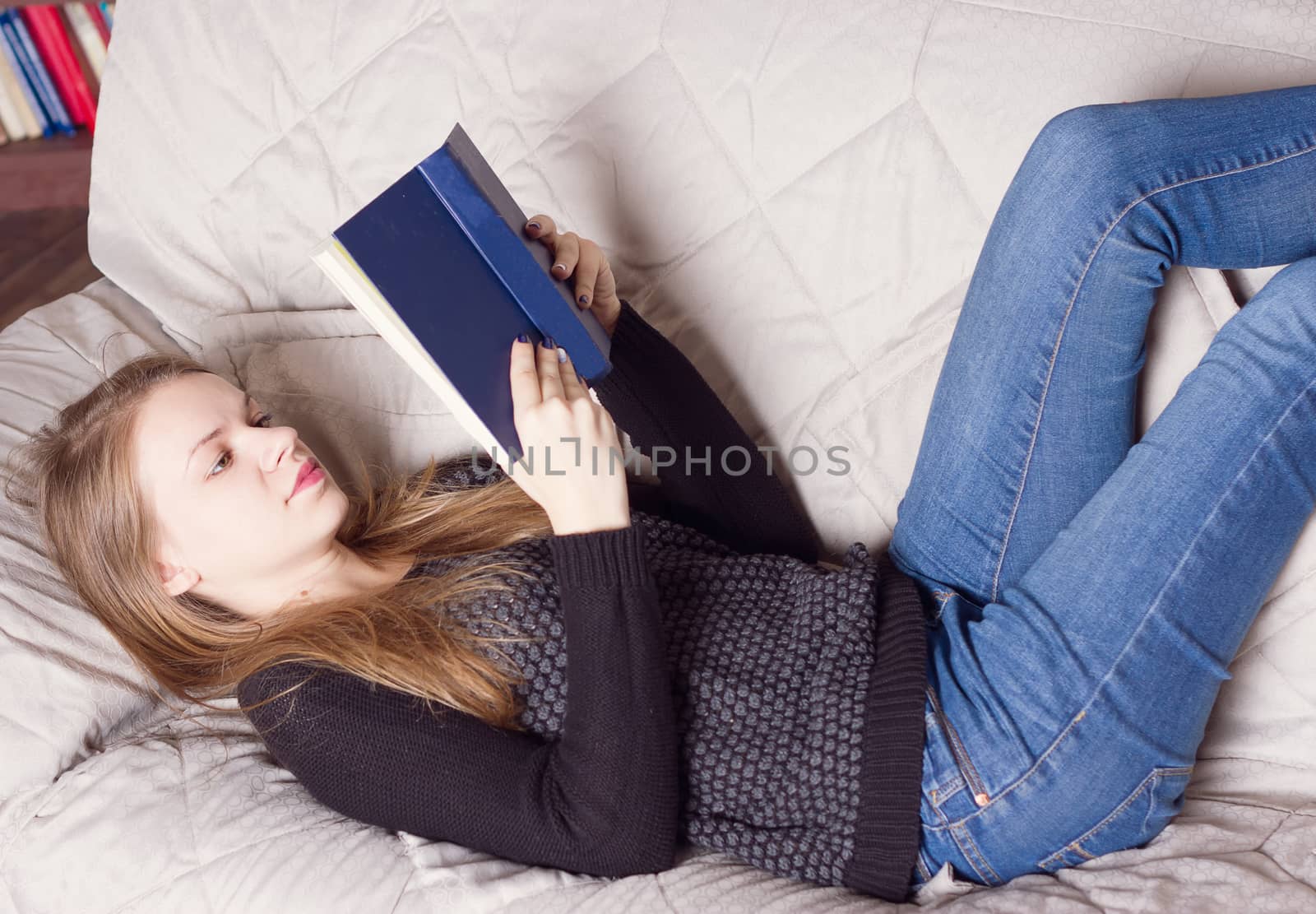 Beautiful young blond woman reading book on the bed at home