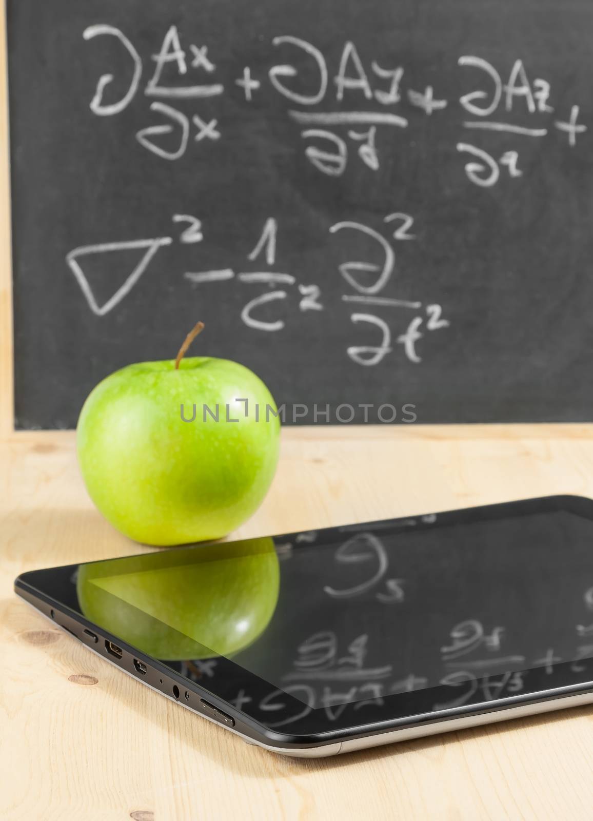 tablet pc and green apple in front of blackboard on wood table, concept of learn new technology
