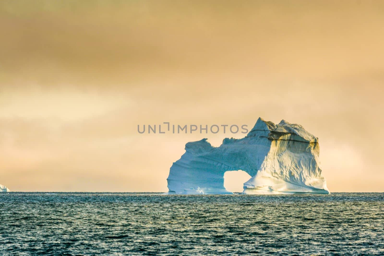 A rugged and powerful iceberg with an "O" floats in the blue Arctic ocean.