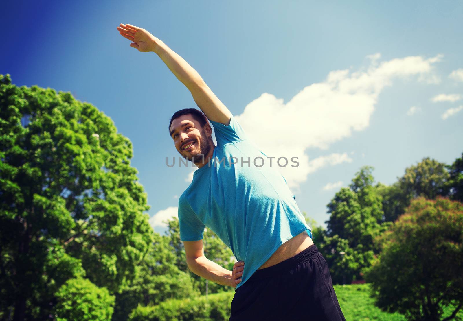 fitness, sport, training and lifestyle concept - smiling man stretching hand outdoors