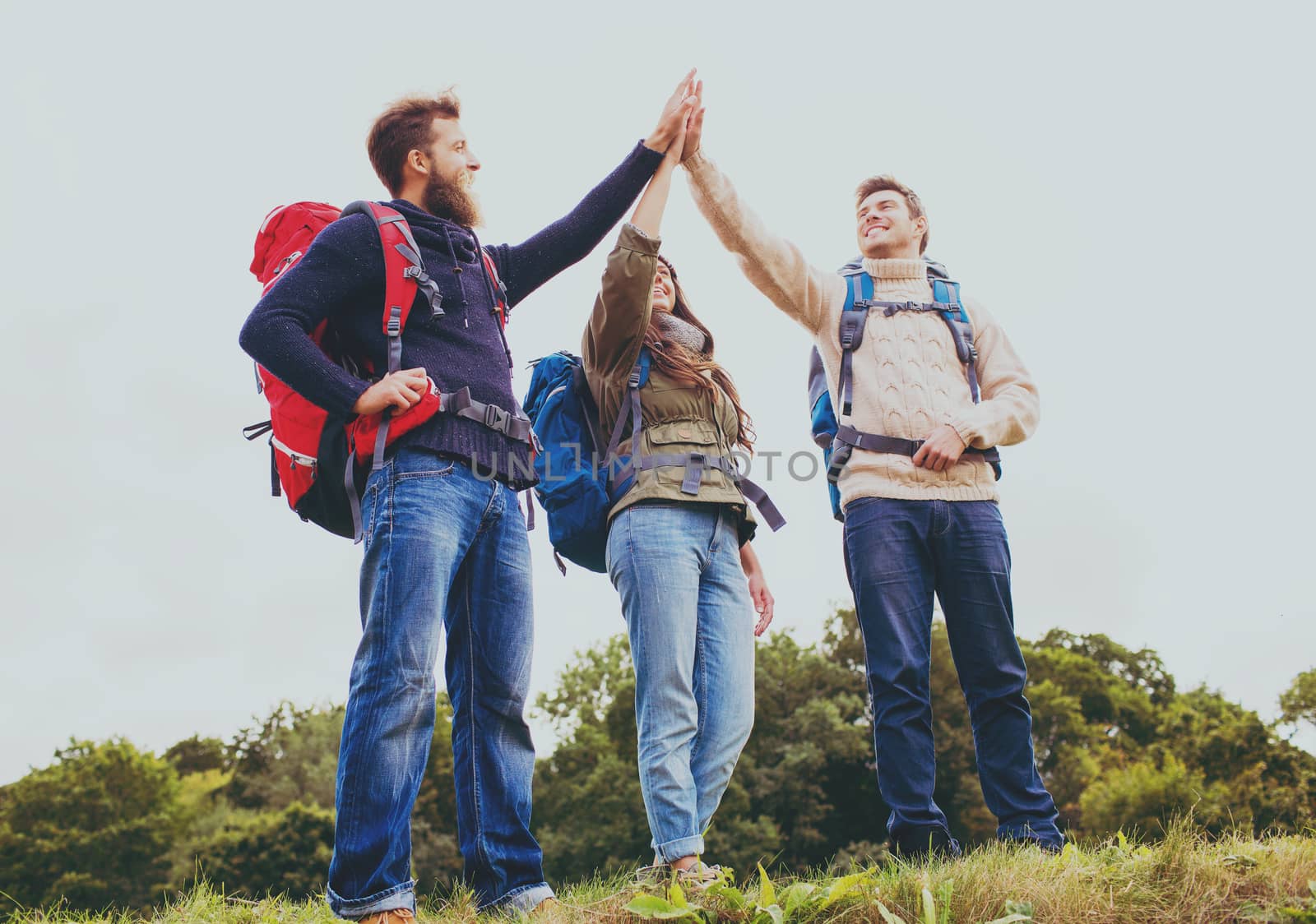 travel, tourism, hike, gesture and people concept - group of smiling friends with backpacks making high five outdoors