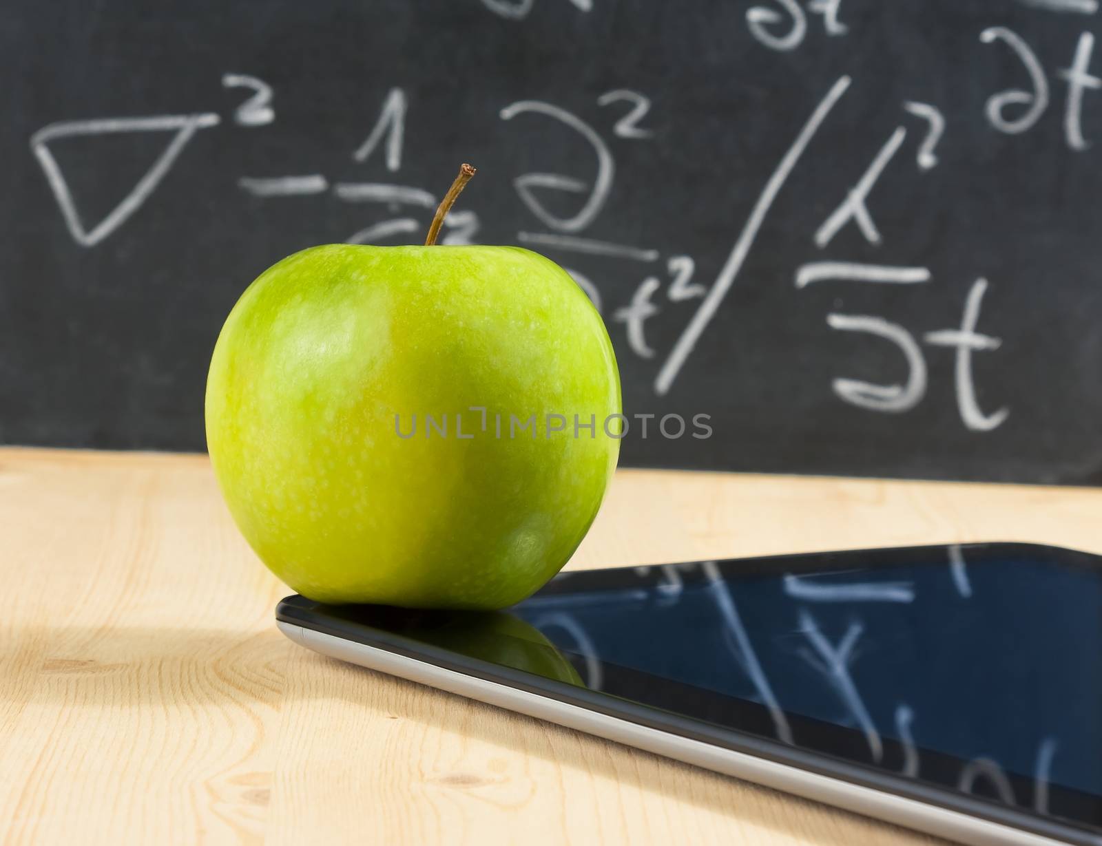 digital tablet pc and green apple in front of blackboard on wood table by donfiore