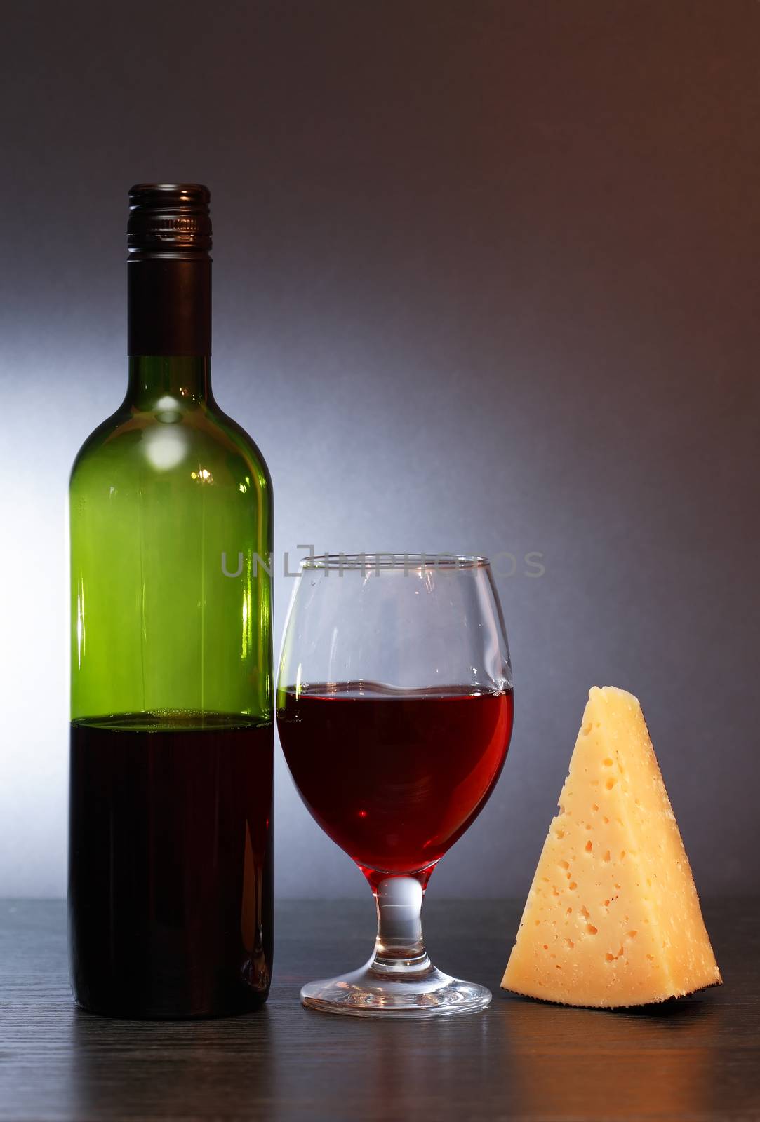 Bottle of red wine near wineglass and piece of cheese on nice gray background