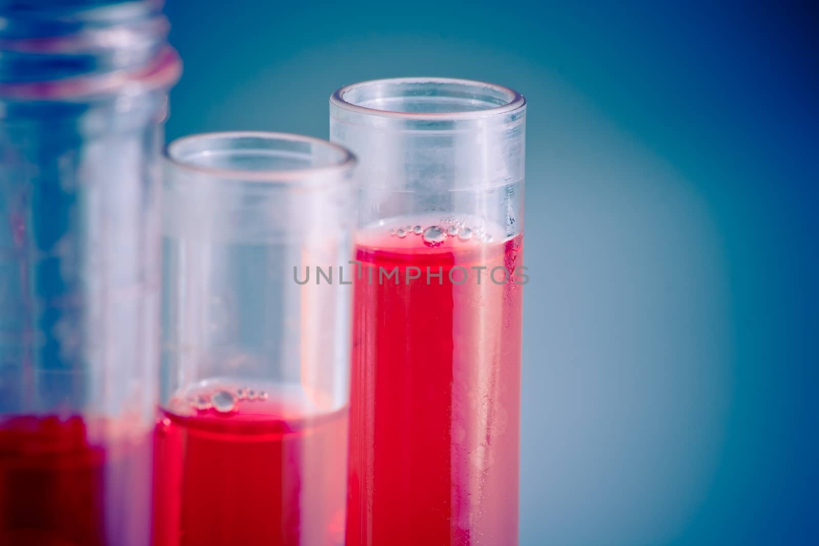 test tubes with red liquid in laboratory on blue light tint background with space for text